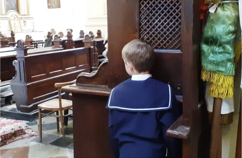 Chłopiec klęczy w konfesjonale